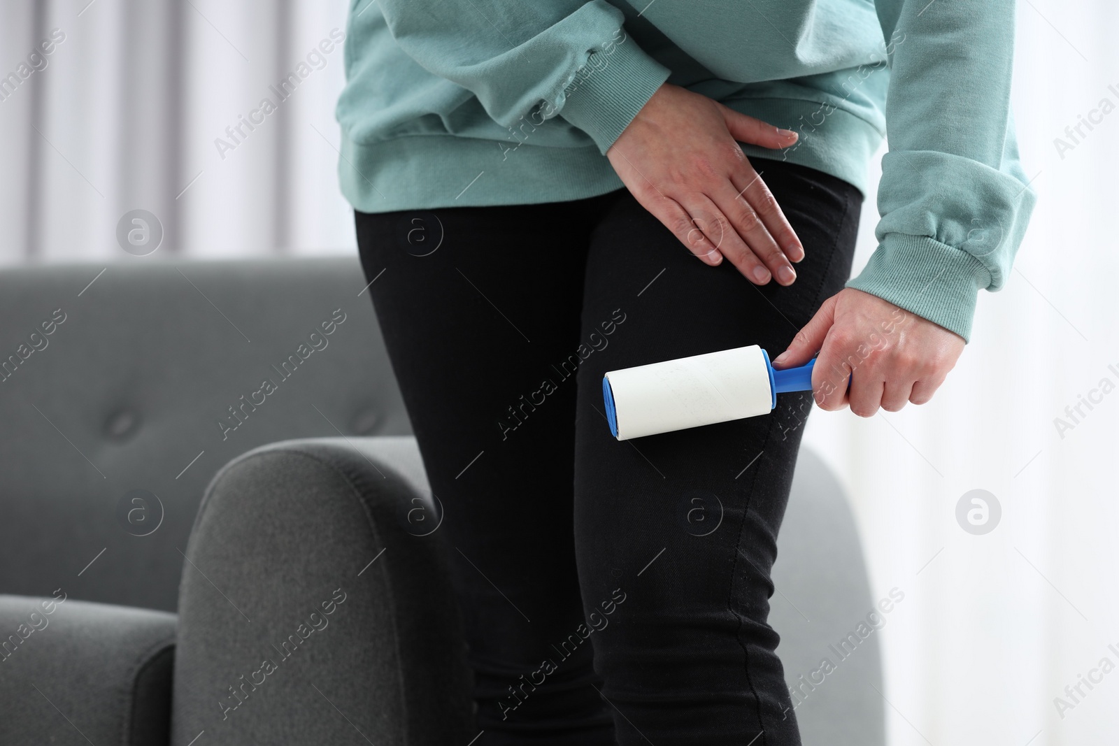 Photo of Woman with lint roller removing pet hair from black trousers indoors, closeup