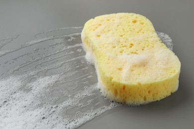 Yellow sponge with foam on grey background, closeup