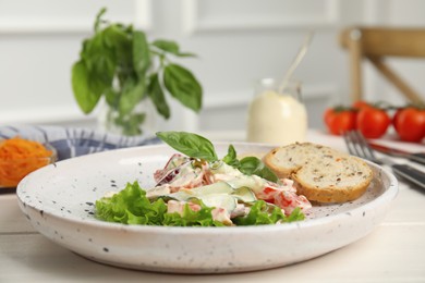 Photo of Plate of delicious vegetable salad dressed with mayonnaise and croutons on white table, closeup