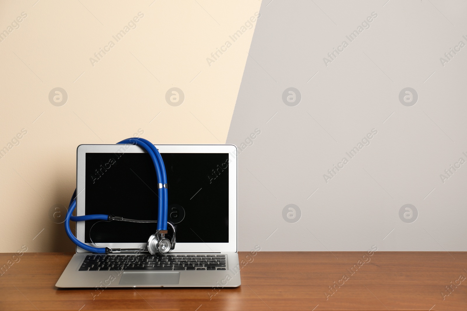 Photo of Modern laptop with stethoscope on table against color wall. Mockup for design