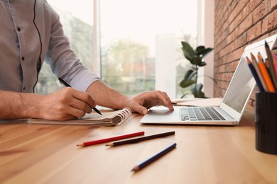 Photo of Man drawing in notebook at online lesson indoors, closeup. Distance learning