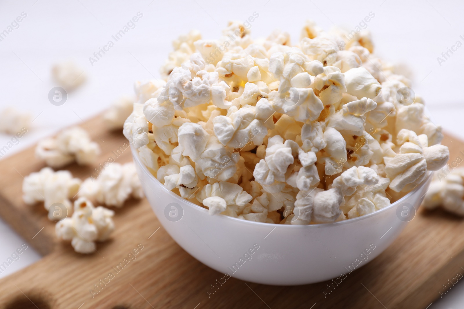Photo of Tasty popcorn in bowl on wooden board, closeup