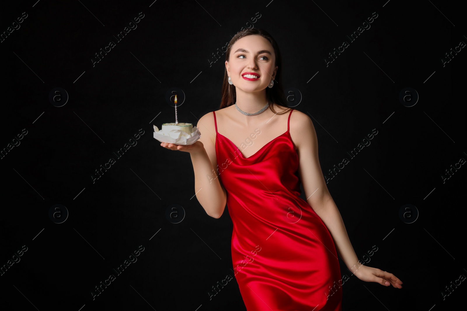 Photo of Attractive young woman holding her Birthday cake with burning candle on black background