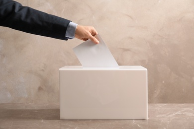 Man putting his vote into ballot box on color background, closeup