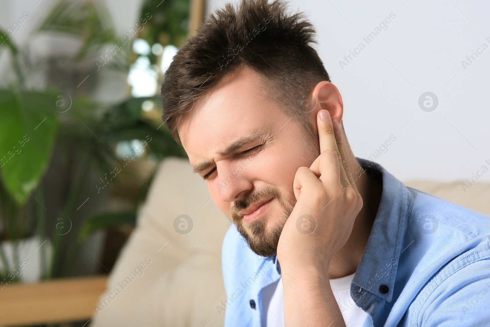 Photo of Young man suffering from ear pain at home. Space for text