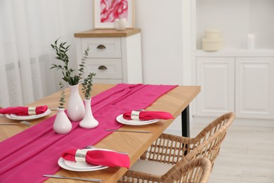 Beautiful table setting and vases with green branches in dining room