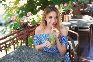 Photo of Young woman with glass of tasty lemonade at table in cafe, outdoors. Natural detox drink