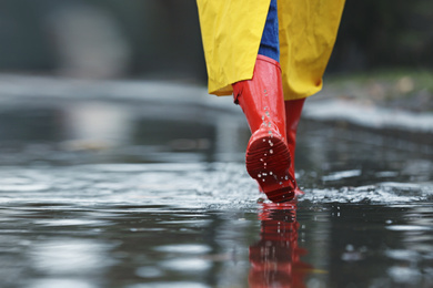 Photo of Woman in rubber boots walking outdoors on rainy day, closeup. Space for text