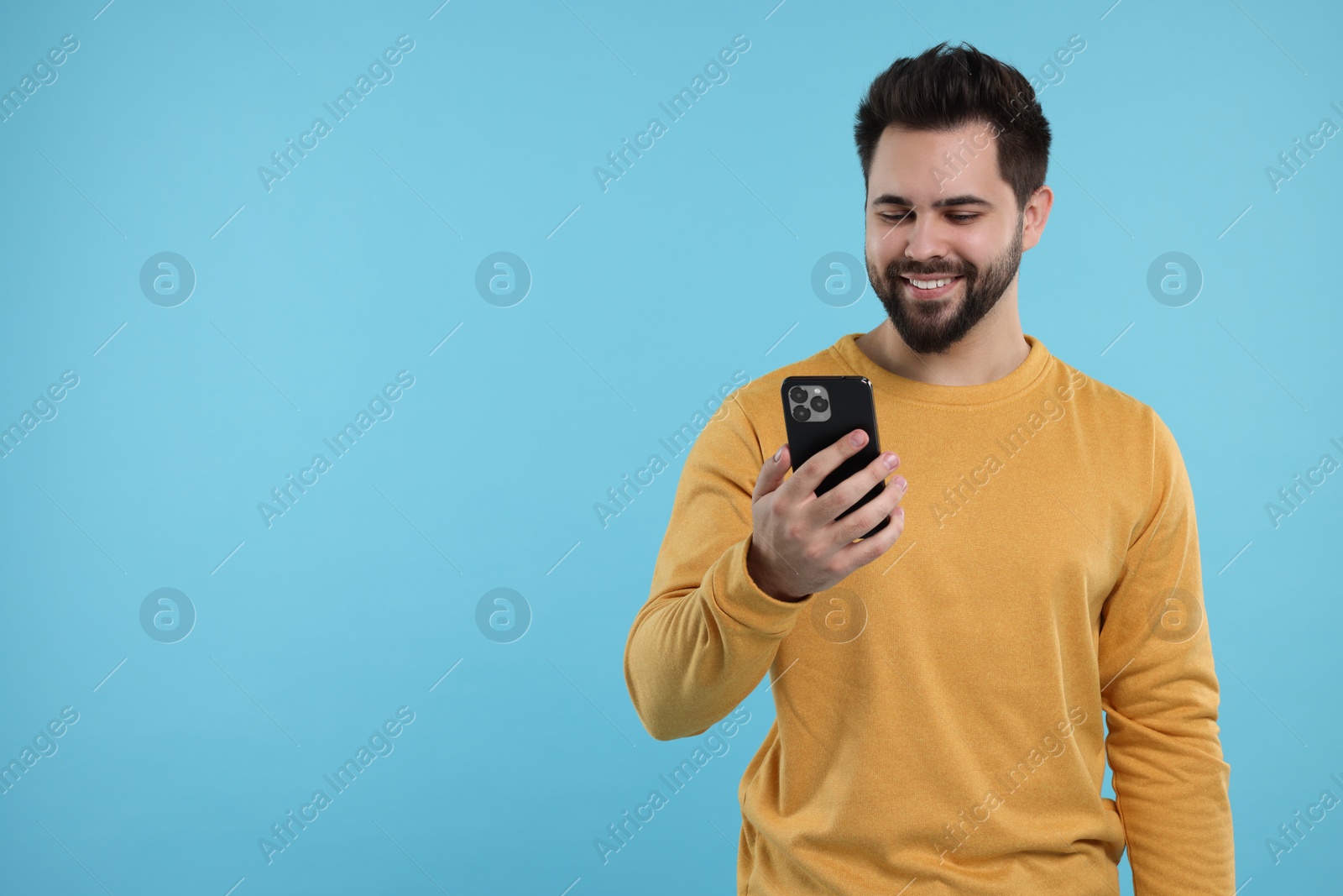 Photo of Happy young man using smartphone on light blue background, space for text