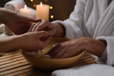 Photo of Woman receiving hand massage in spa salon, closeup. Bowl of water and flowers on wooden table