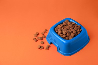 Photo of Dry pet food in feeding bowl on orange background. Space for text