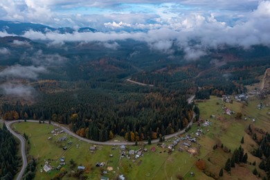 Image of Aerial view of beautiful forest, road and mountain village on autumn day