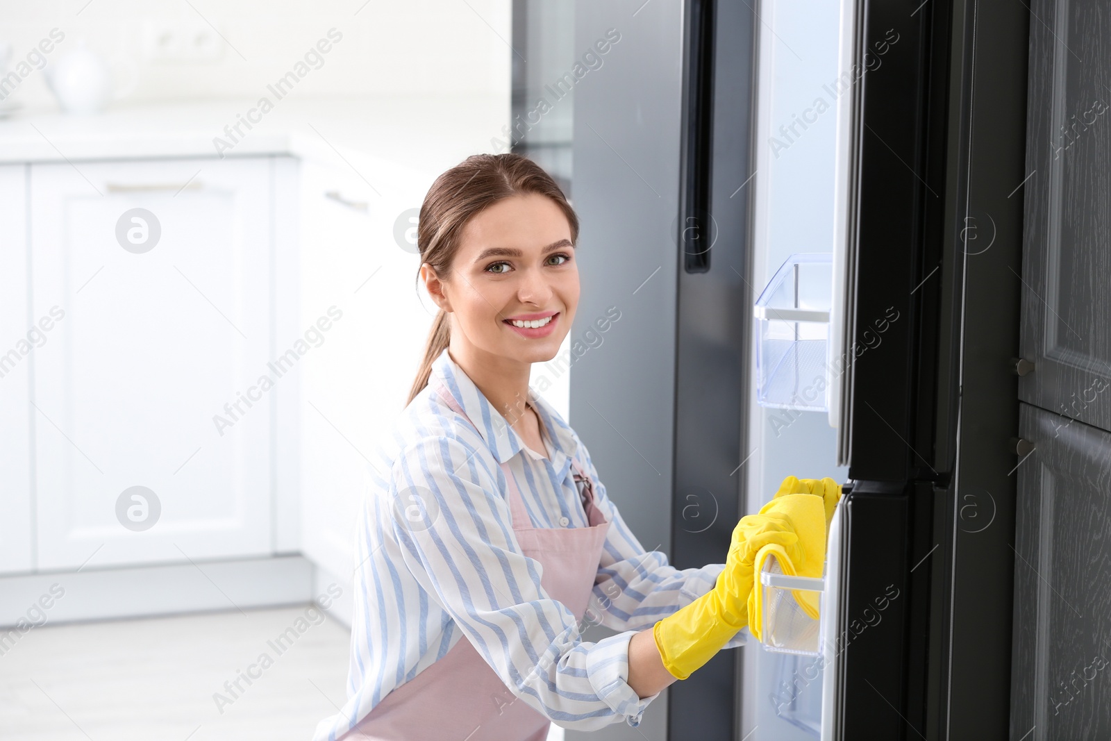 Photo of Woman in rubber gloves cleaning refrigerator at home