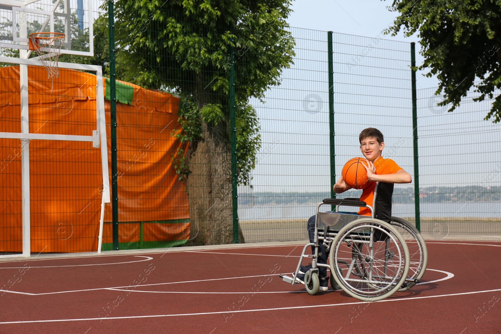 Photo of Disabled teenage boy in wheelchair playing basketball  on outdoor court