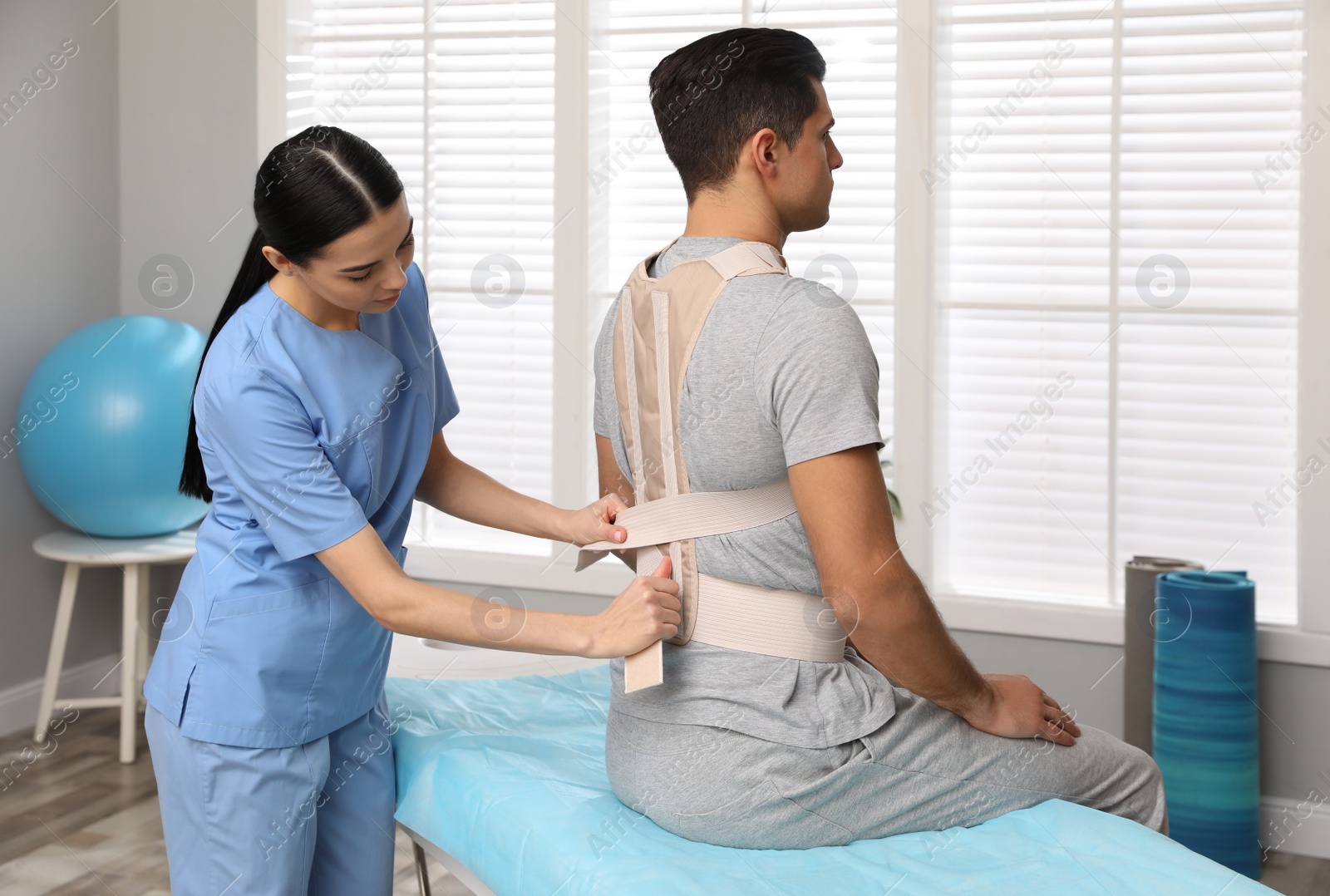 Photo of Orthopedist helping patient to put on posture corrector in clinic. Scoliosis treatment