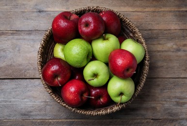Photo of Fresh ripe green and red apples with water drops in wicker bowl on wooden table, top view