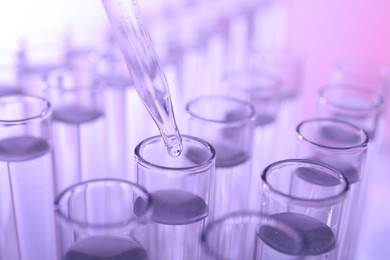 Dripping liquid from pipette into test tube on violet background, closeup