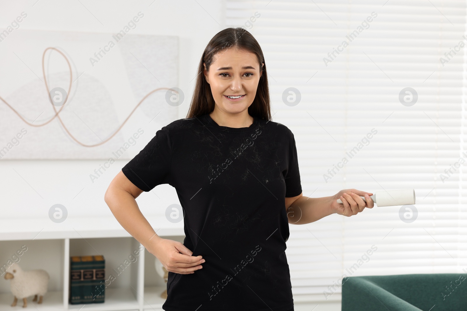 Photo of Emotional woman with lint roller and pet hair on her black clothers at home