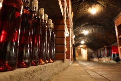 Photo of Beregove, Ukraine - June 23, 2023: Many bottles of red wine on shelves in cellar, low angle view