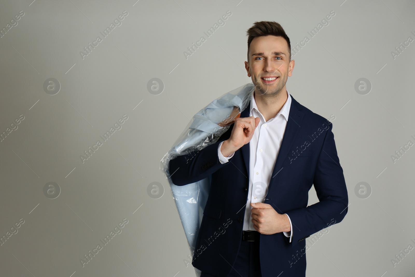 Photo of Man holding hanger with shirt in plastic bag on light grey background. Dry-cleaning service