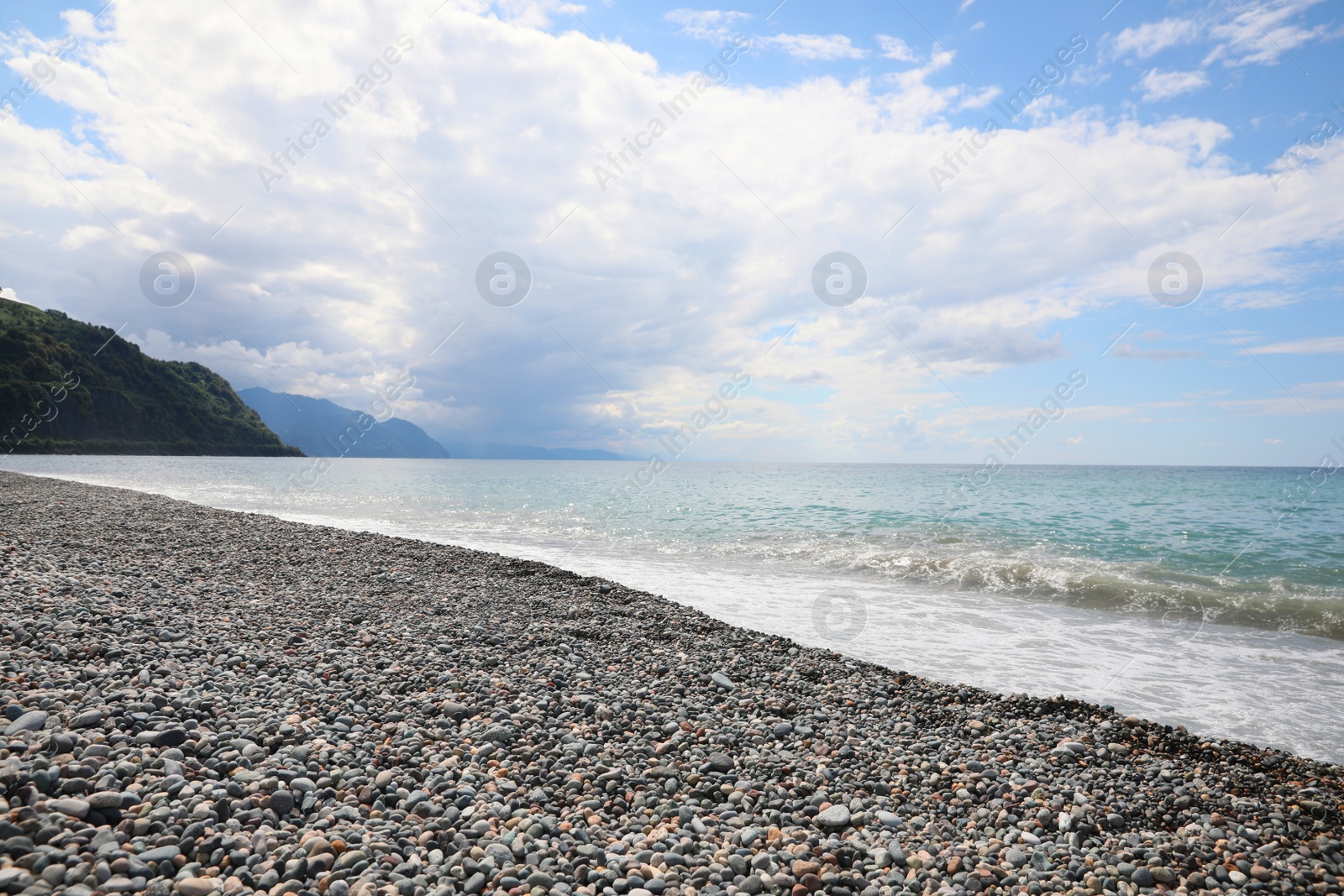 Photo of Picturesque view of beautiful sea shore and hills under sky with fluffy clouds