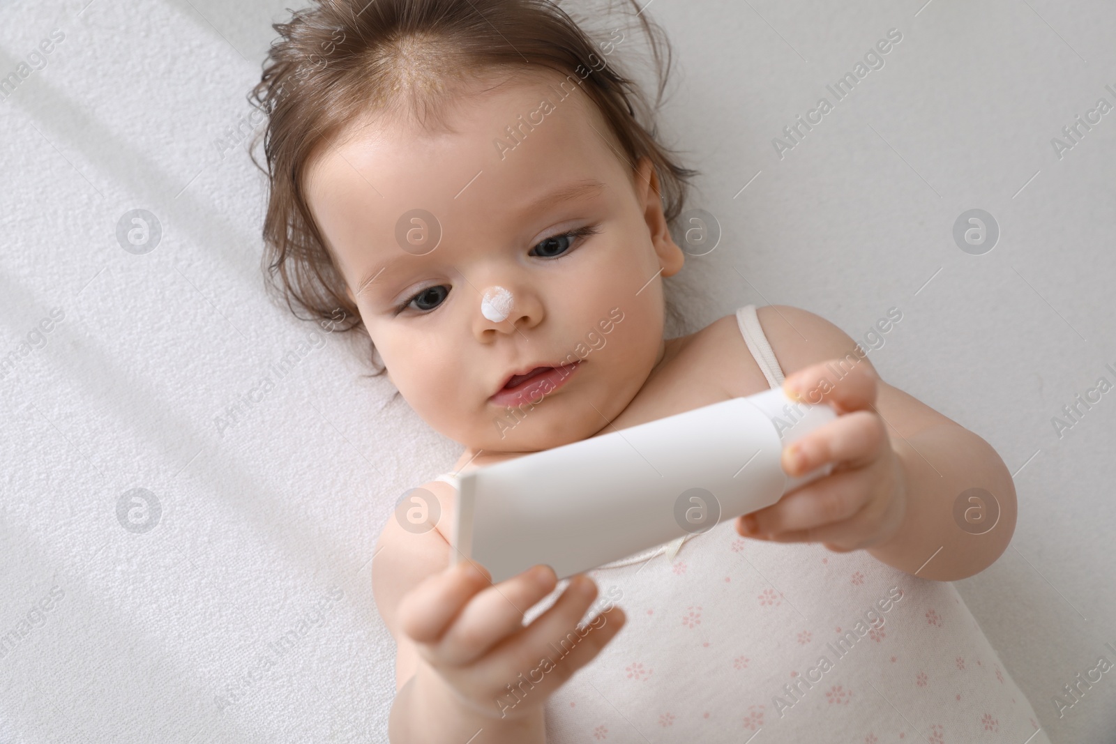 Photo of Cute little baby with cream in comfortable crib, top view