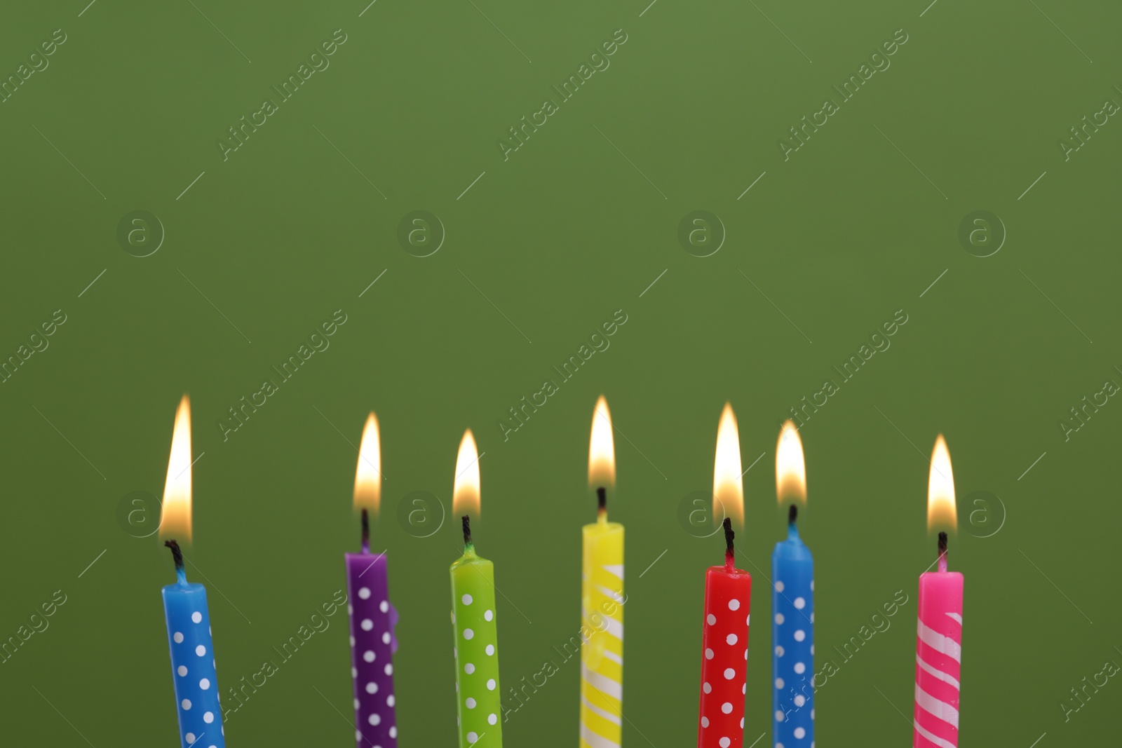Photo of Many burning candles on green background, closeup. Birthday celebration