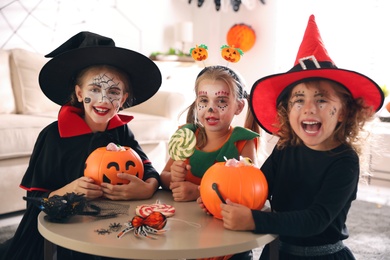 Photo of Cute little kids with pumpkin candy buckets wearing Halloween costumes at home