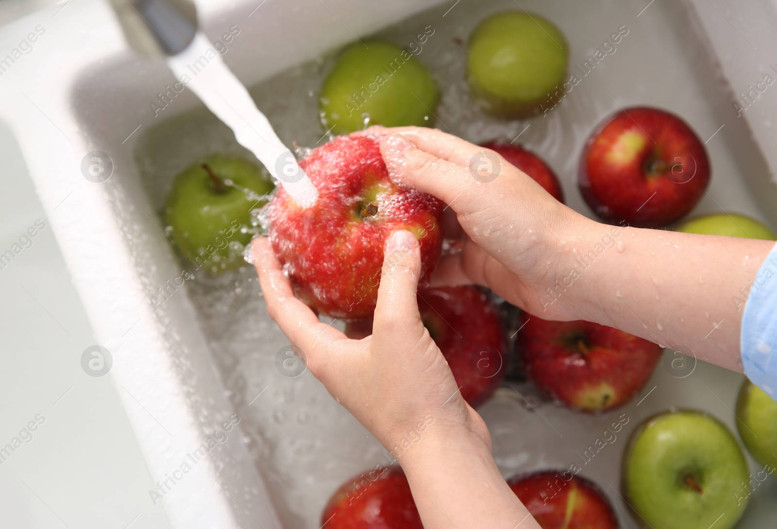 Photo of Woman washing fresh apples in kitchen sink, top view