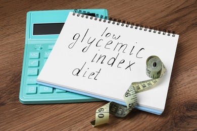 Photo of Notebook with words Low Glycemic Index Diet, measuring tape and calculator on wooden table
