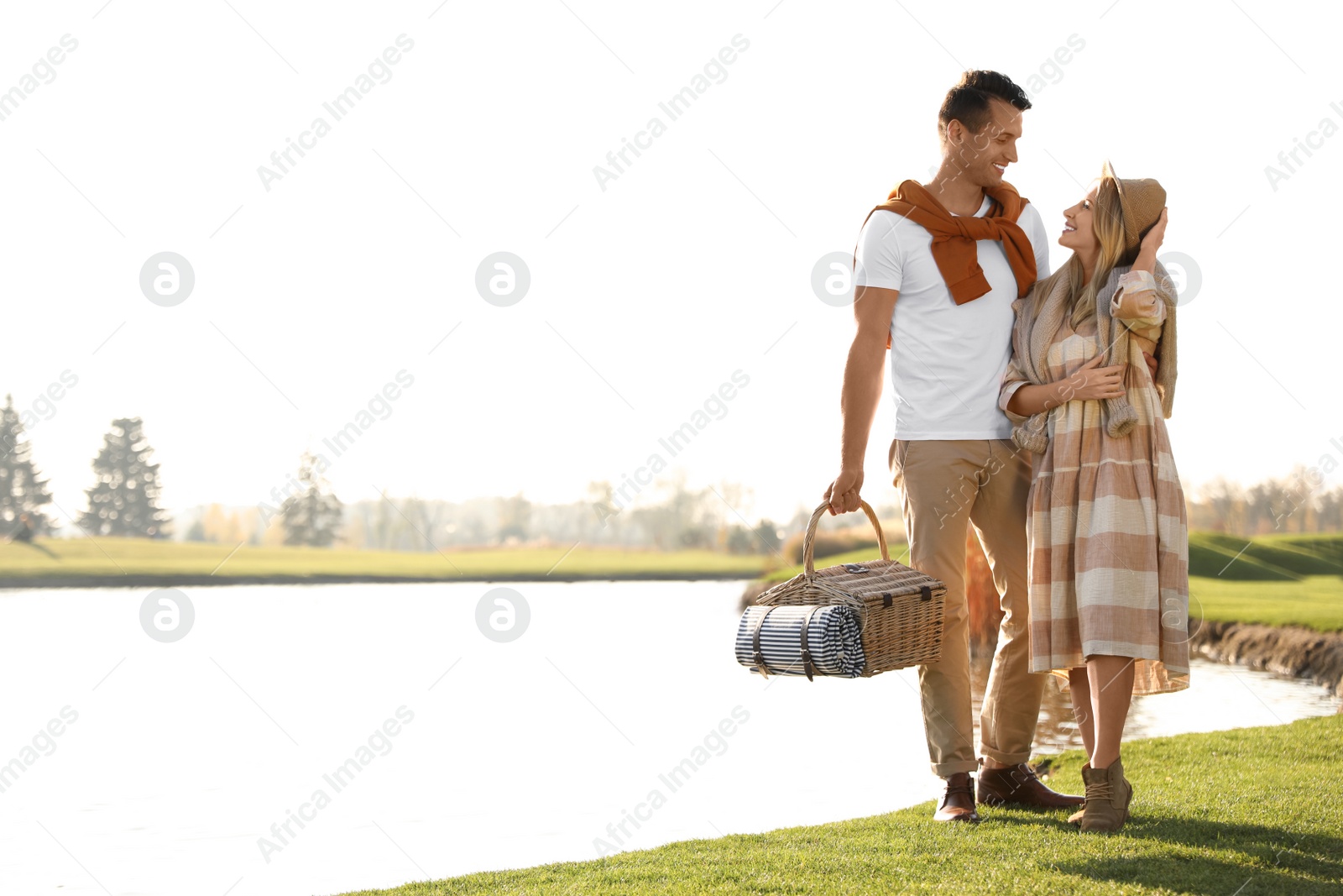 Photo of Young couple with picnic basket near lake on sunny day