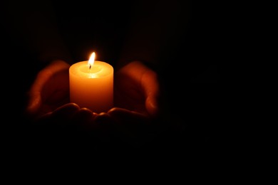 Woman holding burning candle in hands on black background, closeup. Space for text