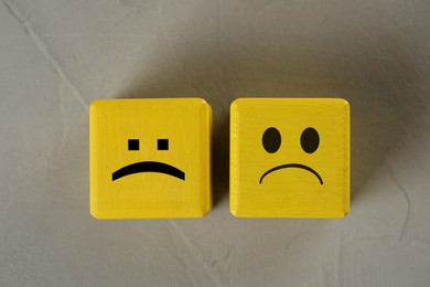 Image of Yellow cubes with sad faces on grey table, top view