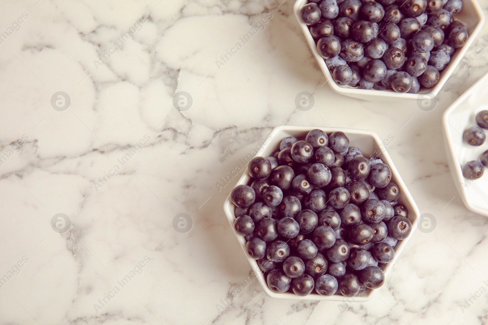 Photo of Bowls with fresh acai berries on marble table, top view