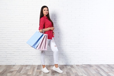 Photo of Beautiful young woman with blank paper bags near brick wall, space for text