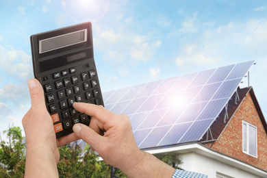 Image of Man using calculator against house with installed solar panels. Renewable energy and money saving