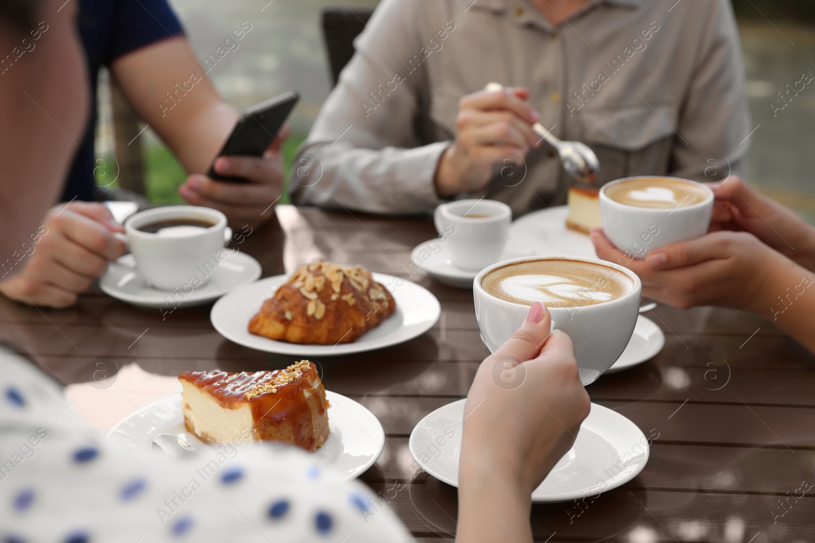 Photo of Friends drinking coffee at wooden table in outdoor cafe, closeup