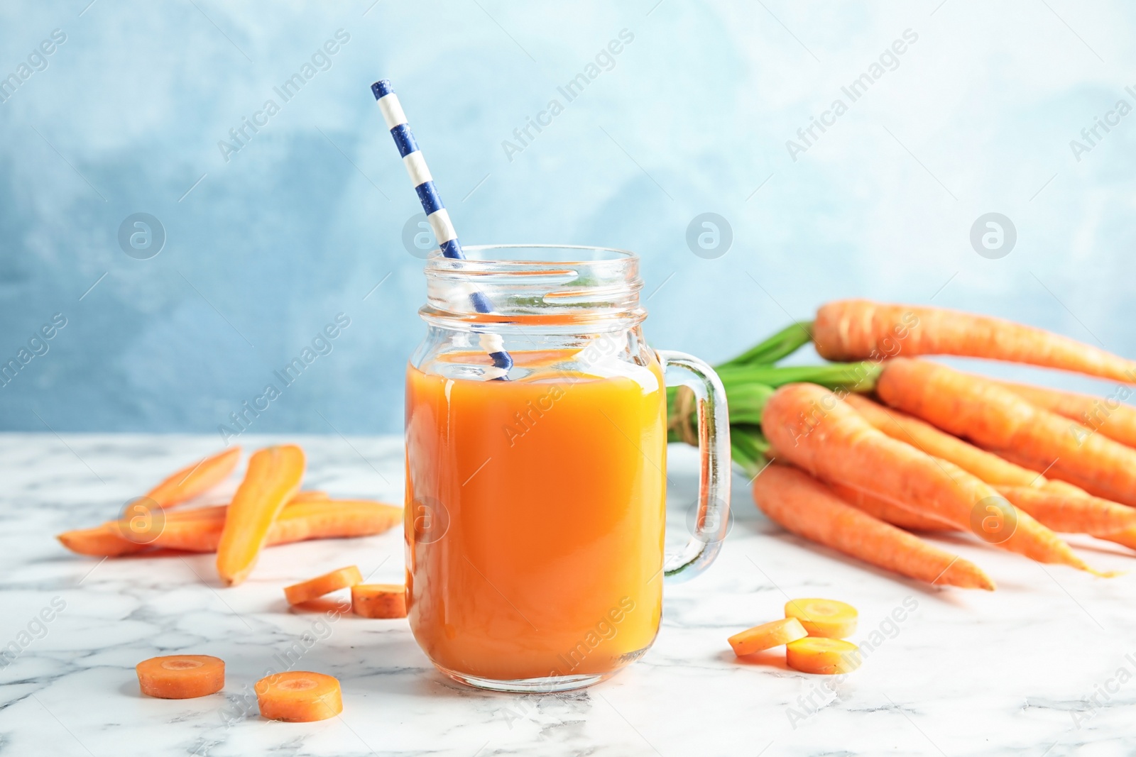 Photo of Mason jar with carrot juice and fresh vegetable on table