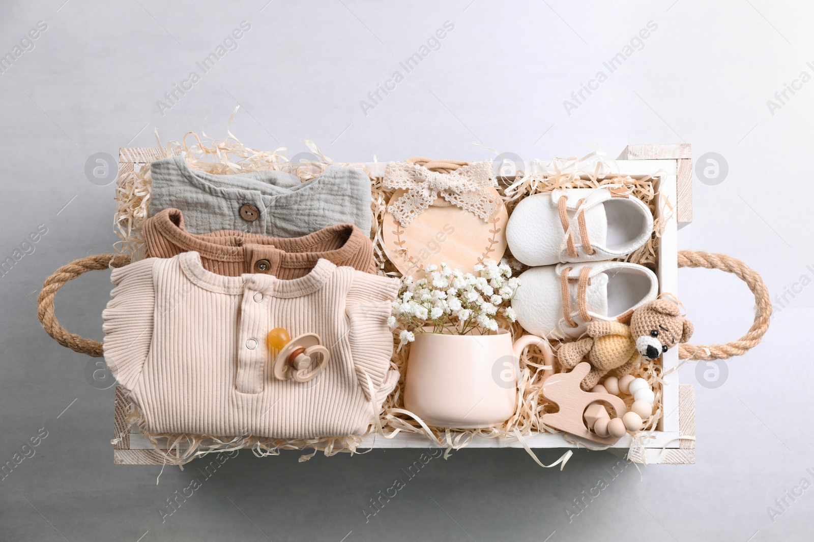 Photo of Wooden box with baby clothes, booties and toys on grey background, top view