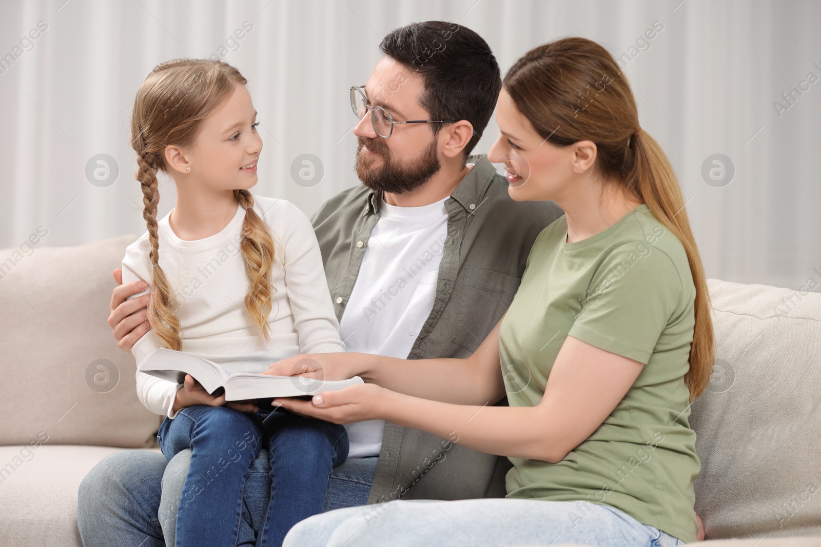 Photo of Girl and her godparents reading Bible together on sofa at home