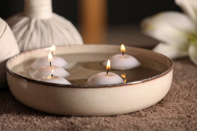 Photo of Burning candles in bowl with water on massage table, closeup