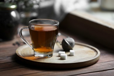 Photo of Tray with cupfreshly brewed tea and sugar cubes on wooden table indoors