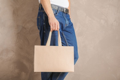 Man holding mock-up of paper shopping bag on color background