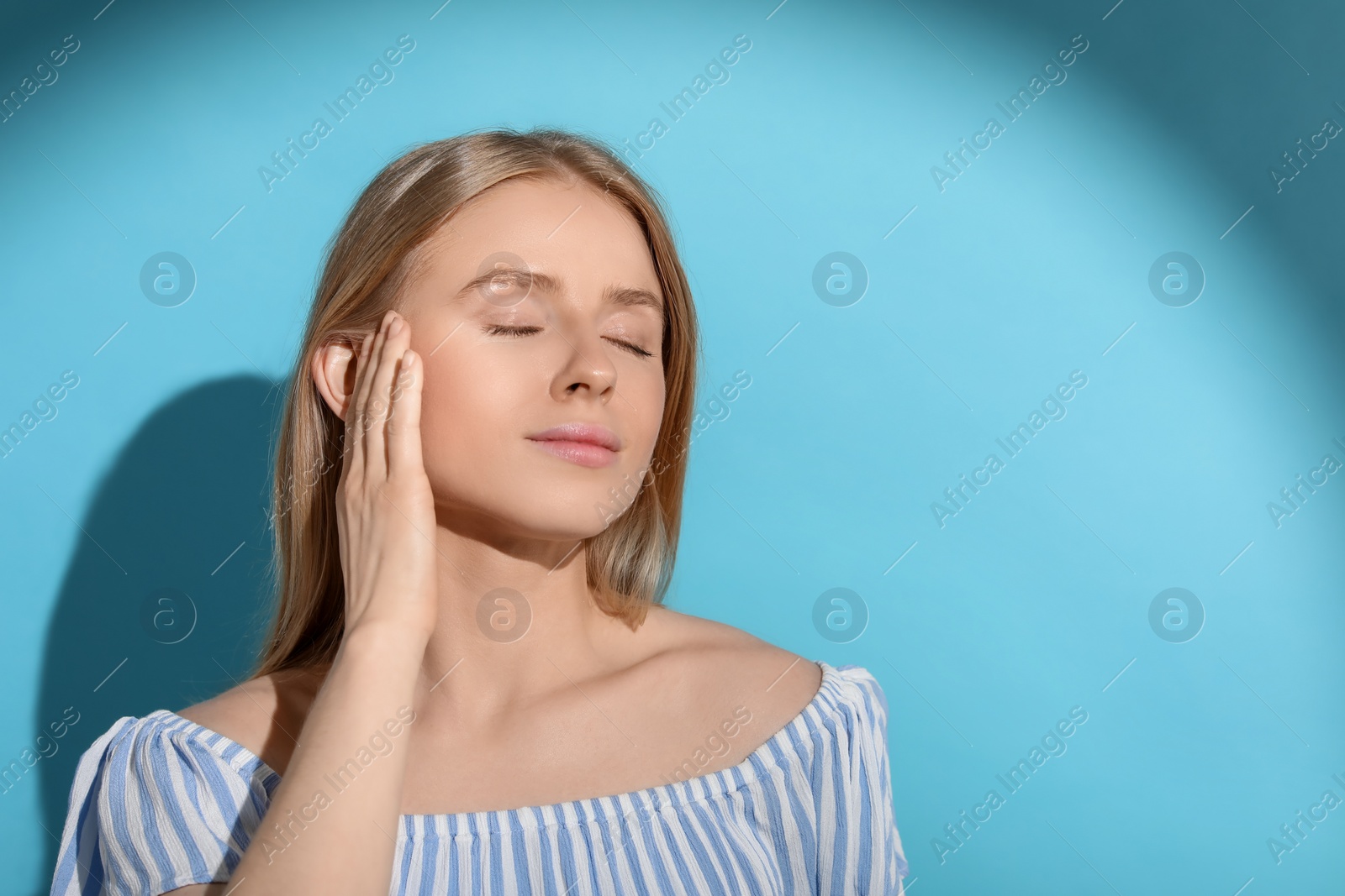 Photo of Beautiful young woman in sunlight on light blue background, space for text