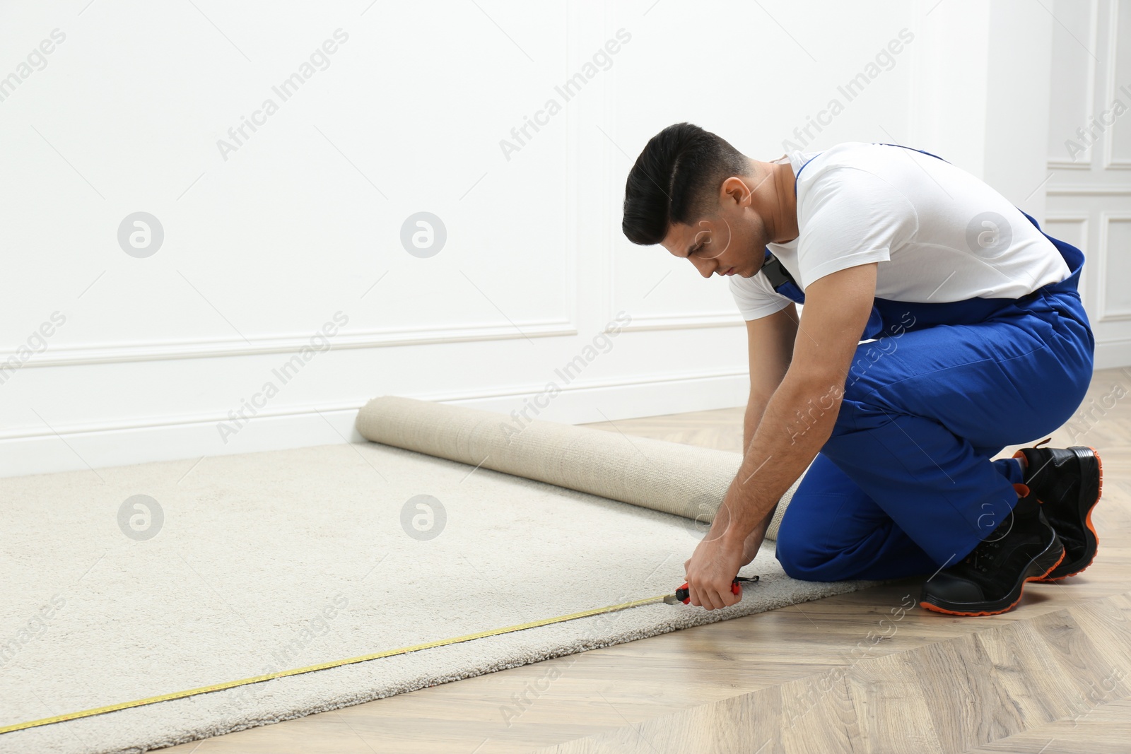 Photo of Worker with measuring tape installing new carpet indoors