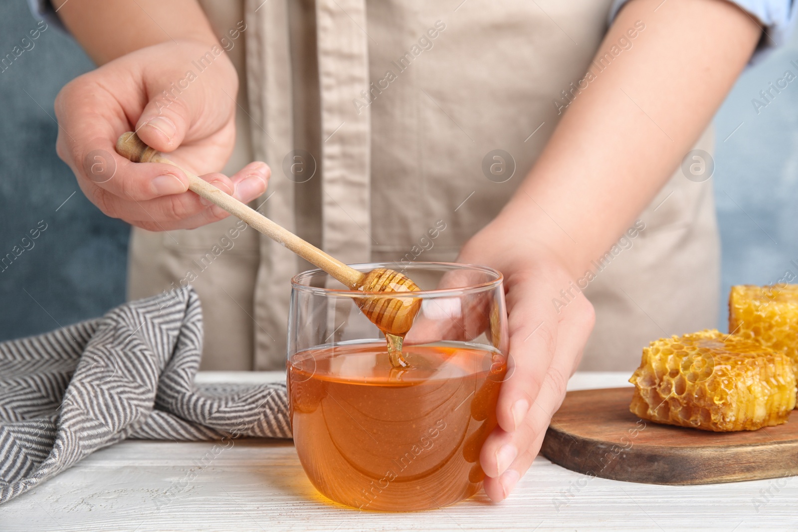 Photo of Woman with honey and dipper at white wooden table, closeup