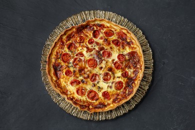 Photo of Delicious homemade quiche with prosciutto and tomatoes on black textured table, top view