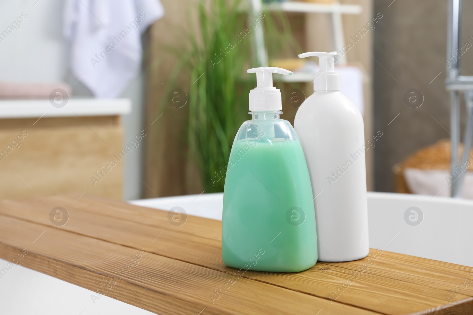 Photo of Wooden bath tray with bottles of shower gels on tub indoors, space for text