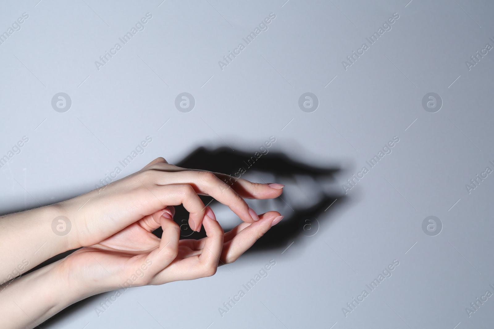 Photo of Shadow puppet. Woman making hand gesture like crocodile on grey background, closeup. Space for text