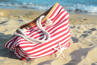 Photo of Stylish striped bag with dry starfish on sandy beach near sea